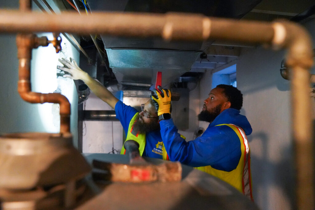 Two technicians from Chimney Scientists inspect a water heater and its chimney in a home in Norristown, PA, as part of carbon monoxide detection services
